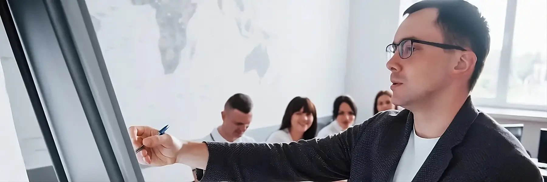 Una persona escribiendo en una pizarra con un marcador, de espaldas a la c谩mara hacia la pizarra. Otras personas est谩n sentadas de espaldas a la c谩mara, sugiriendo un aula o sala de reuniones.